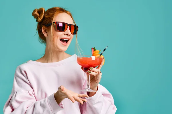 Menina loira alegre em óculos de sol vermelhos modernos com coquetel trópico margarita de morango se diverte conversando com amigos gesticulando — Fotografia de Stock