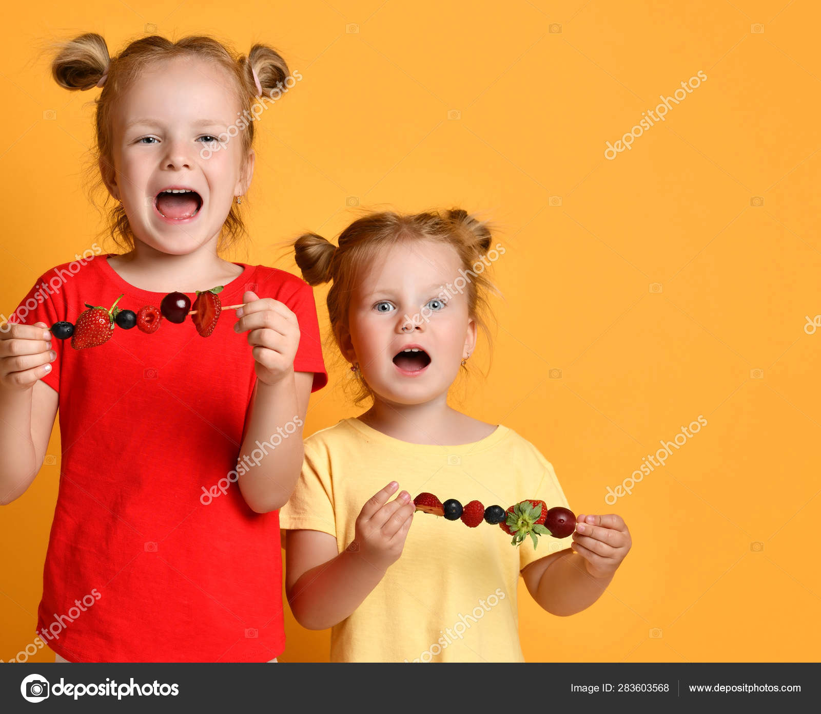 Two kids sisters happy smiling screaming eating fruit skewers dessert