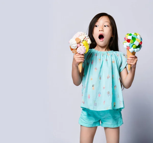 Sorprendida asiática bebé niña con dos grandes helados en conos de gofres con sabrosos ingredientes —  Fotos de Stock