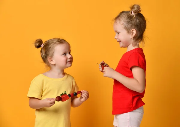 Две сестры счастливо улыбаются, крича, поедая фруктовый шашлык десерт с ягодами вишневой клубничной черники — стоковое фото