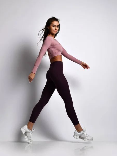 Joven atlética chica morena en buena forma en ropa deportiva de moda caminando en uniforme de gimnasio hace ejercicios de cardio — Foto de Stock