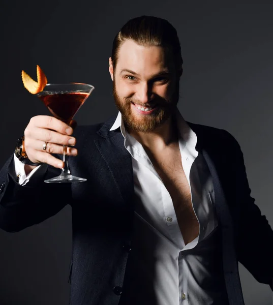 Stylish modern man bearded clubber in fashion suit looks skeptically at the glass with fresh cocktail drink — Stock Photo, Image