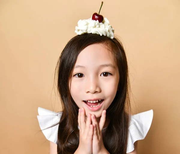 Jeune fille asiatique enfant avec doux dessert cerise sur la tête sur un beige — Photo