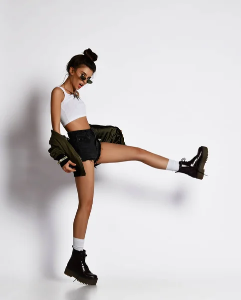 黒いブーツとグレーの緑のジャケットで脚を打つスポーツウェアの戦闘機の若いスポーティな女の子 — ストック写真