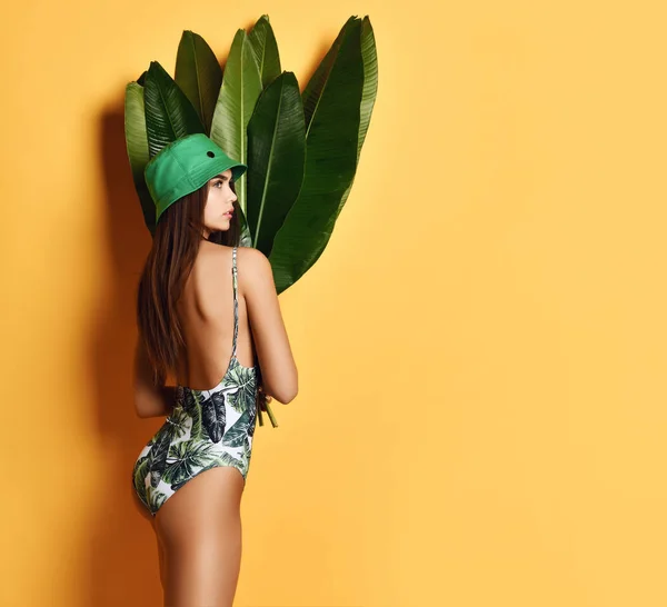 Mooie jonge Fashion Girl met perfecte huid in groene hoed houden tropische bananenblad in handen en covers — Stockfoto