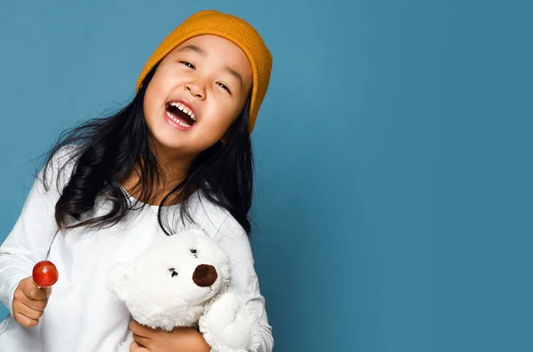 Азиатская девочка держит игрушку белого медведя и конфетку леденец счастливо улыбаясь крича — стоковое фото