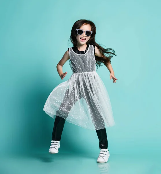 Cheerful stylish asian baby girl kid in modern black and white clothes and sunglasses dances at party jumps having fun