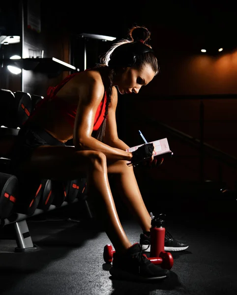 Sporty woman fitness trainer is writing down results in dairy planning practice. Diet and weight loss concept