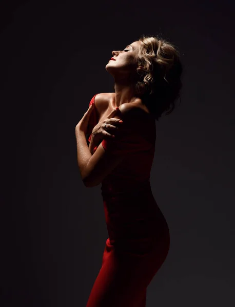 Mooie trendy vrouw met krullend haar en emoties in rode jurk poseren op donker — Stockfoto