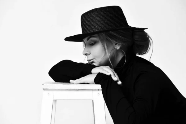 Черно-белый портрет грустной женщины в черной шляпе с краями и водолазкой, лежащей головой на руках на белом — стоковое фото
