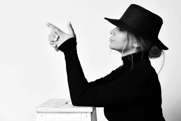 Retrato preto e branco no perfil de mulher loira de chapéu preto com aba fazendo um gesto de pistola apontando para algo — Fotografia de Stock