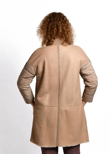 Mujer modelo pelirroja posa con su espalda a nosotros en elegante abrigo de piel de oveja beige combinado con mangas textiles —  Fotos de Stock