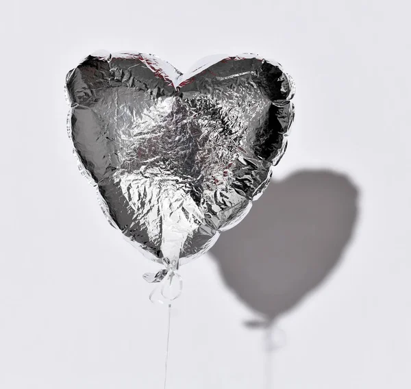 Вечеринка над сдутым серебристым сердечным шаром объект на белом сером фоне с тенью — стоковое фото