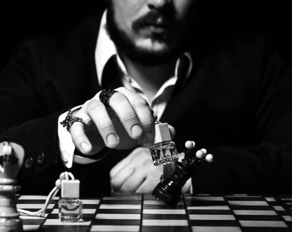 Homem brutal em terno oficial e anéis elegantes jogando xadrez com garrafa de perfume, fazendo um movimento, ataque rainha preta — Fotografia de Stock