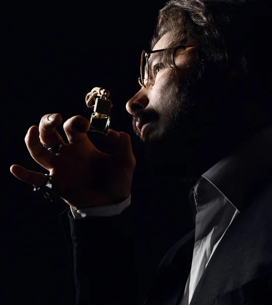 Brutal man master perfumer with beard and modern hairstyle wearing glasses smell small perfume bottle