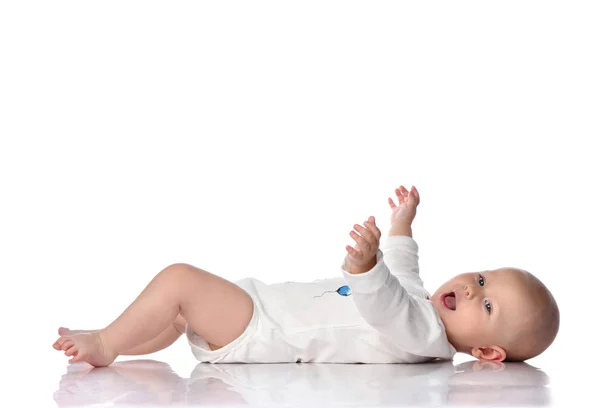 Riendo bebé niño pequeño en traje de cuerpo blanco está acostado en su espalda, sosteniendo las manos, saludando, feliz gritando en blanco —  Fotos de Stock