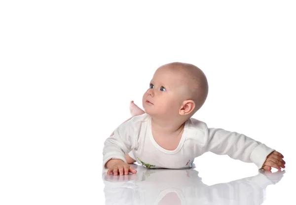 Curioso bebé bebé niño en traje de cuerpo blanco está acostado sobre su estómago mirando hacia arriba en el espacio libre de copia cerca de él en blanco —  Fotos de Stock