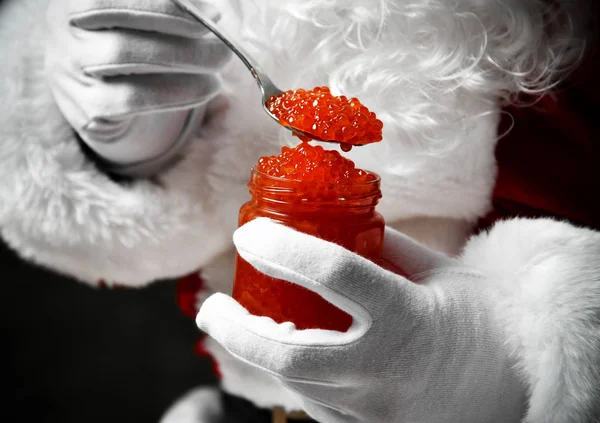 Primo piano del barattolo pieno e cucchiaio di caviale di salmone rosso nelle mani di Babbo Natale in guanti bianchi. Anno nuovo e Buon Natale — Foto Stock