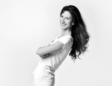 Beyaz tişörtlü, dar kotlu, zayıf gülümseyen bir kadının siyah beyaz portresi kollarını kavuşturarak poz veriyor.