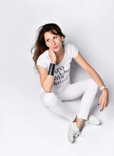 View from above. Slim woman in white tight clothes is sitting cross-legged on the white floor, looking aside — Stock Photo, Image