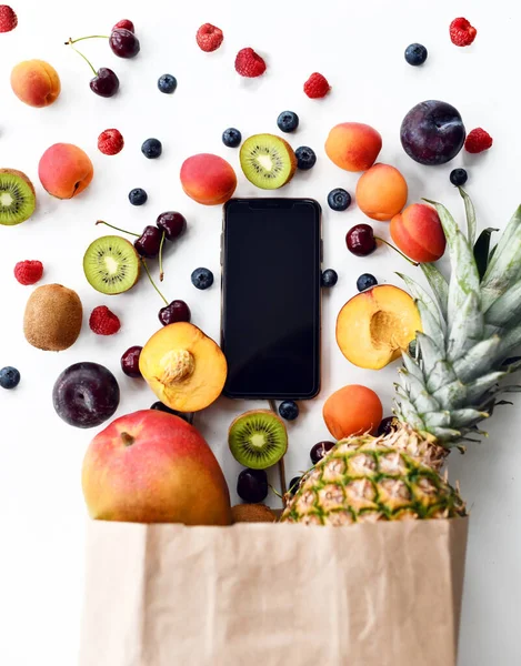 Obst und Beeren Frühstück Lieferung Zusammensetzung Blaubeere Himbeere Kirschen Kiwi und Mobiltelefon mit leerem Bildschirm — Stockfoto