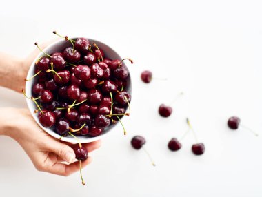 Bir kase dolusu taze kiraz meyvesi kadının ellerinde ve etrafa saçılmış. Sağlıklı yemek için organik süper gıda kavramı 