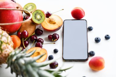 Yabanmersini, kiraz, kayısı, ananas, mango ve kivi ile çevrili akıllı telefon.