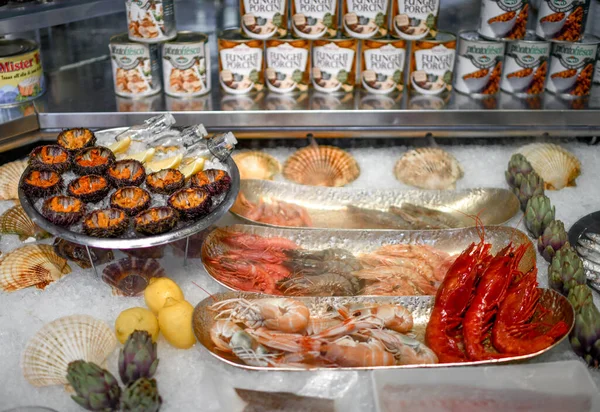 Poissonnerie avec différents fruits de mer. Assiettes aux grosses crevettes fraîches savoureuses, oursin décoré d'artichauts — Photo