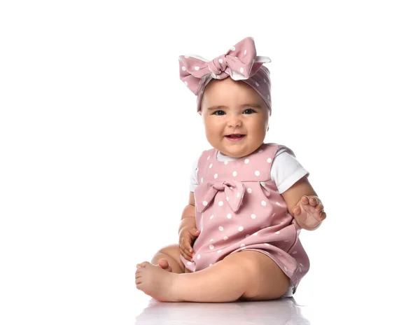 Smiling Infant baby toddler in polka dot dress and headband with bow sits on the floor holding hand up — Stock Photo, Image