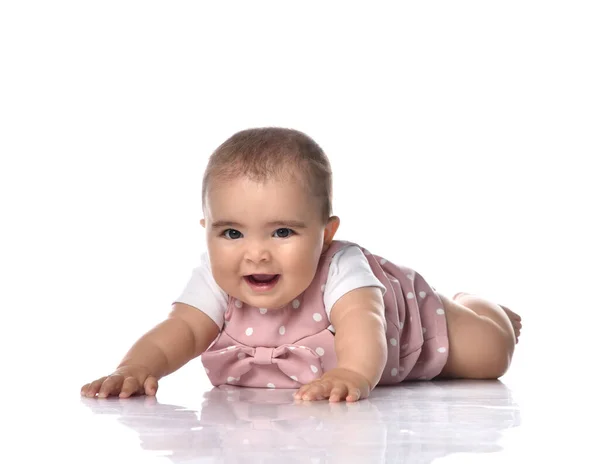 Happy infant baby girl toddler in polka dot dress is lying on stomach on the floor with arms outstretched tries to crawl — Stock Photo, Image