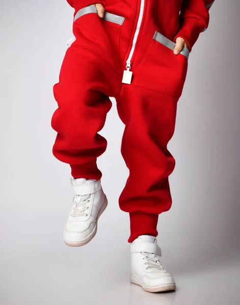 Κοντινό πλάνο του παιδιού σε κόκκινο συνολικό jumpsuit και λευκά sneakers στέκεται ανύψωση πόδι για να βήμα πάνω — Φωτογραφία Αρχείου