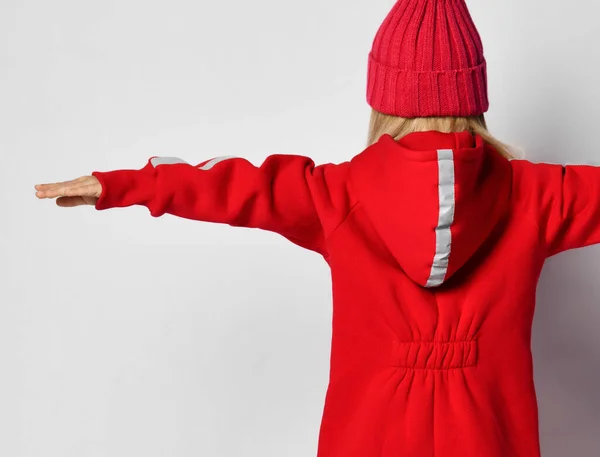 Jeune fille blonde en combinaison rouge et chapeau d'hiver se tient à nous avec ses bras écartés large — Photo