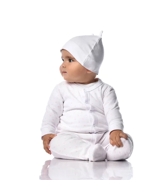 Cute smiling infant baby toddler sits on the floor in white onepiece overall and funny hat with ears and looks aside — Stock Photo, Image