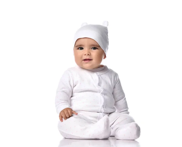 Attentive infant baby toddler in white jumpsuit overall and funny hat sits on the floor listens and tries to understand — Stock Photo, Image
