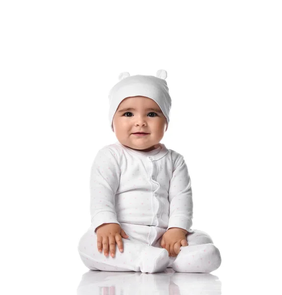 Infant baby toddler sits on the floor in white jumpsuit overall and funny hat with ears touching her legs — Stock Photo, Image
