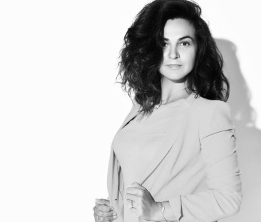 Kendine güvenen kıvırcık esmer kadın modelinin siyah beyaz portresi şık bir takım elbise içinde ceketin yakalarını tutuyor.