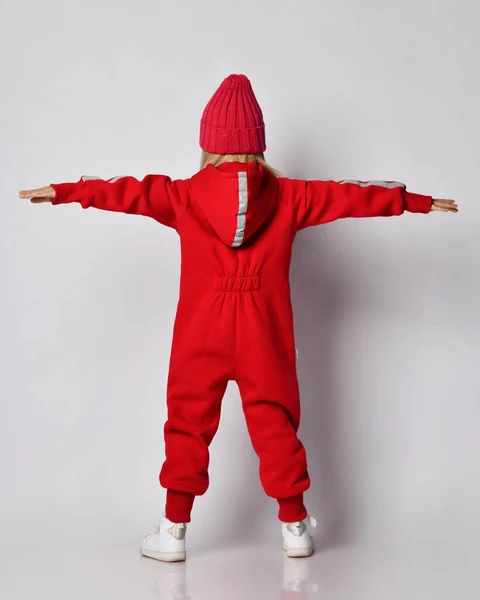 Sarışın, kırmızı tulumlu, kışlık şapkalı, kolları açık bir kız. Arka plan — Stok fotoğraf