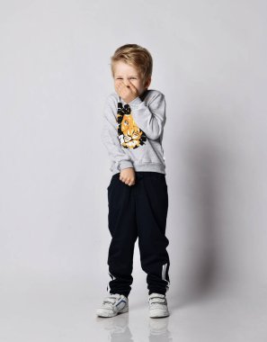 Siyah pantolonlu ve gömlekli sarışın çocuk. Aslan desenli kıkırdıyor. Ağzını ve burnunu eliyle kapatıyor.