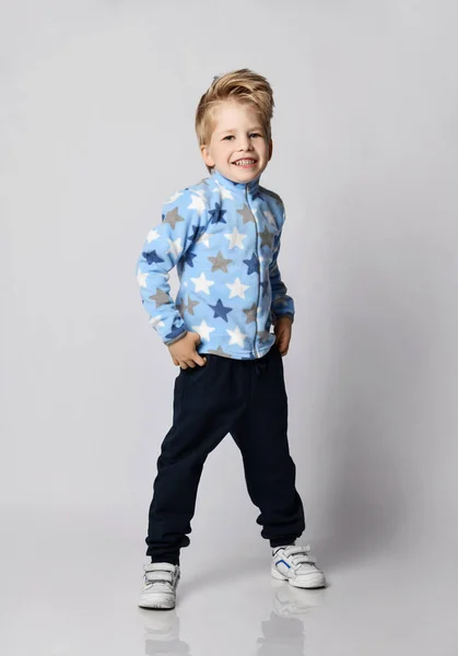 Активный счастливый улыбающийся блондин мальчик в синих штанах, свитер из шерсти со звёздами и белые кроссовки — стоковое фото