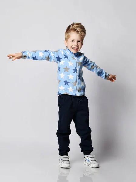 Frolic unge pojke i blå byxor och fleece jacka tröja med stjärnor tryck mönster står med armarna utspridda — Stockfoto