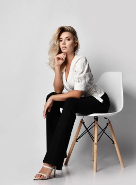Keen attentive young blonde businesswoman in office pantsuit shirt and pants sits on chair leaning forward and looks at camera clipart