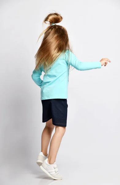Şık gömlekli ve kot etekli aktif bir kız çocuğu zıplayarak ve dönerek eğleniyor. Arka plan — Stok fotoğraf