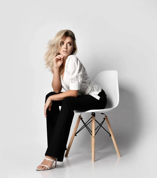 Mladý sexy blondýnka štíhlá žena v kanceláři kalhotový kostým košile a kalhoty sedí na židli naklání dopředu a dívá stranou — Stock fotografie