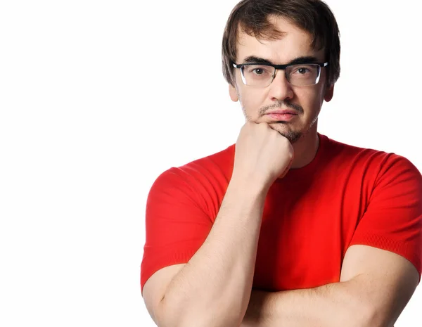 Retrato del hombre reflexivo con gafas y camiseta roja sosteniendo el puño en la barbilla sobre fondo blanco con espacio para copiar —  Fotos de Stock