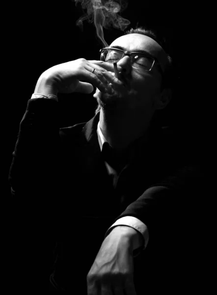 Портрет мужчины в официальном костюме и очках, сидящего и курящего сигарету, приятно держать голову и закрытые глаза — стоковое фото