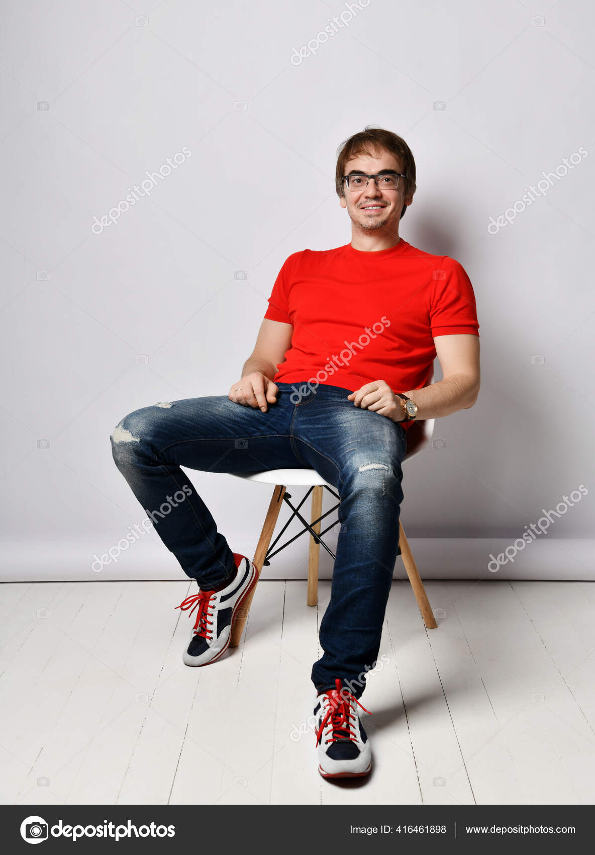 Smiling middle-aged man in red t-shirt, blue jeans, sneakers and