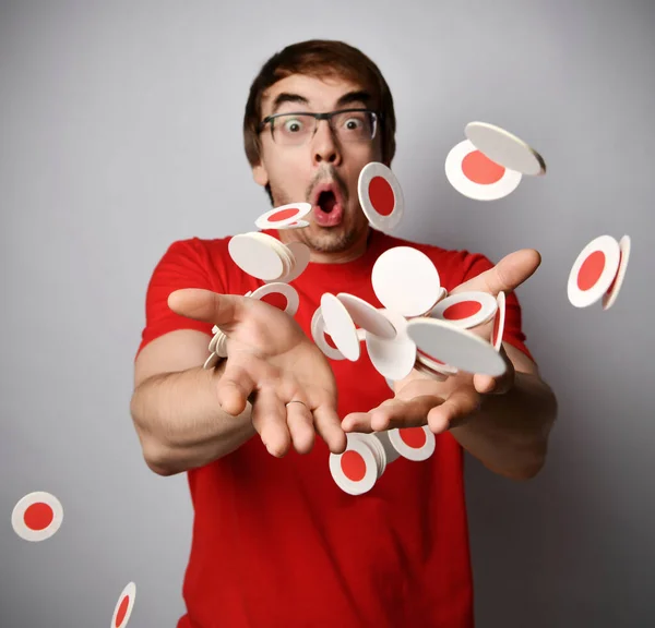 Homem chocado em vermelho t-shirt e óculos trows joga quantidade de branco redondo com beermats vermelhos círculos de papelão — Fotografia de Stock