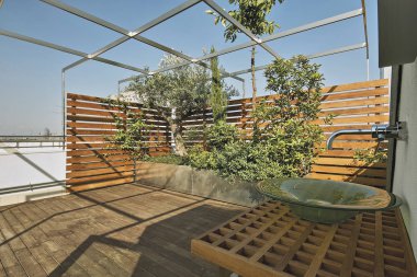 exteriors shots of a modern terrace with hardwood floor and plants into the big planters,  a counter top washbasin on wall clipart