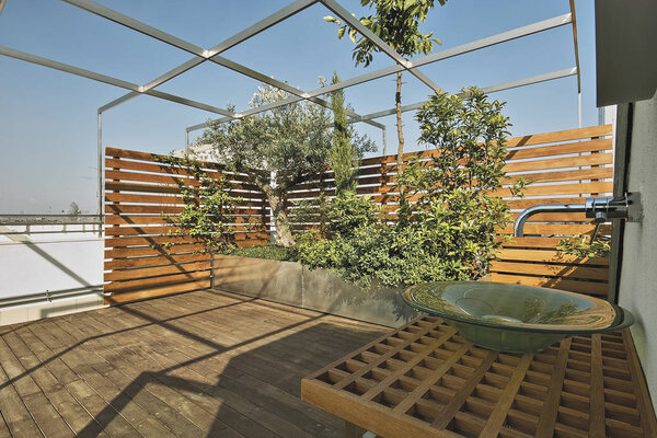 exteriors shots of a modern terrace with hardwood floor and plants into the big planters,  a counter top washbasin on wall