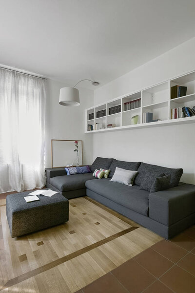 interiors shots of a modern living room whose floor is made of wood in foreground the gray fabric footrest and on the bottom the gray fabric sofa